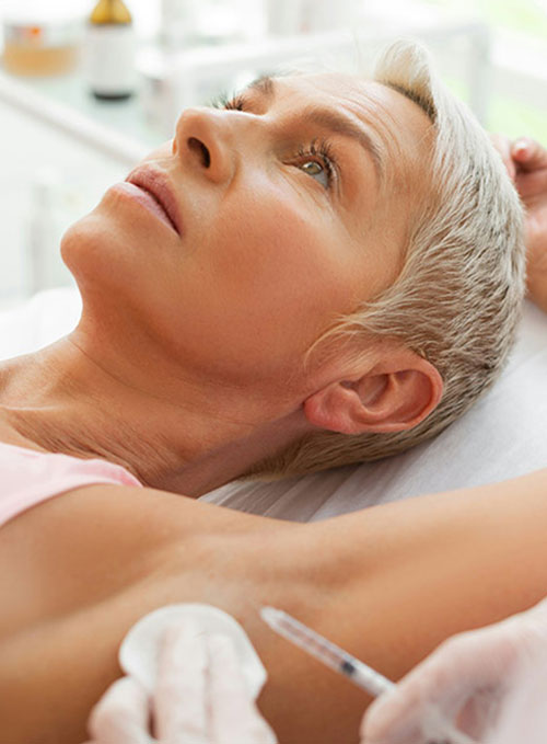 Frau liegt entspannt auf Behandlungsliege, während eine Person mit Handschuhen eine Spritze in ihre Achselhöhle hält